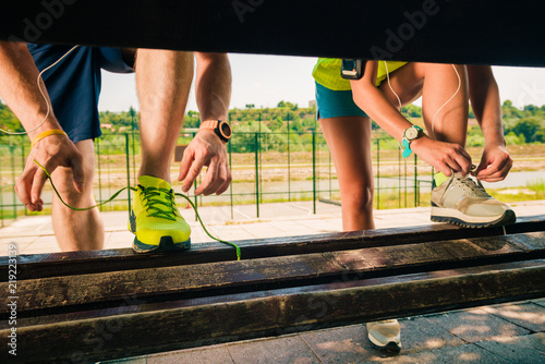 Healthy couple tying their laces of running shoes on bench. Working out in the city urban area.