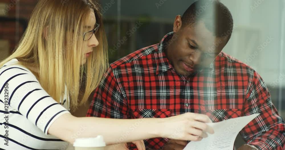 Close up of the young mixed races man and woman reading and flipping pages of the contract in the office room. Close up of the young mixed races man and woman reading and flipping pages of the contract in the office room.