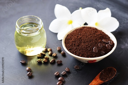 coffee ground scrub with beans, oil and plumeria flowers on black board background, beauty spa concept 