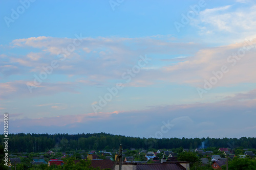 Roofs of houses in a forest village against the background of a dawn or sunset sky.