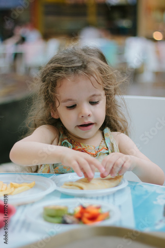 Little kid girl having fun with the food at the cafe or restaurant.