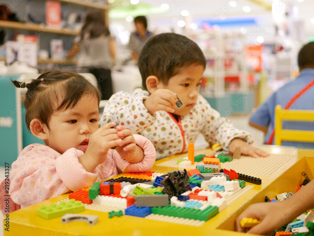 Little Asian baby girl (left) concentrates on pieces of colorful interlocking plastic bricks Little Asian baby girl (left) concentrates on pieces of colorful interlocking plastic bricks