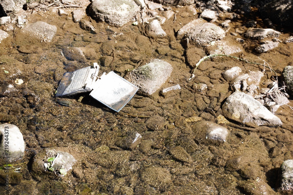 Obraz premium Laptop in the river /Carelessly discarded items pollute the environment and cause problems for all humanity