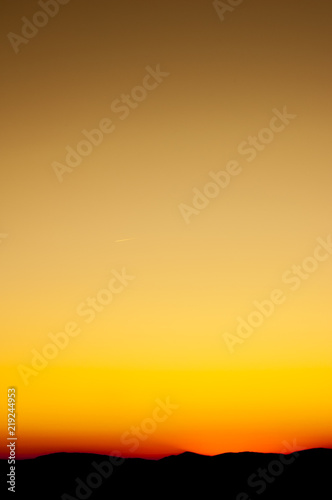 An orange sunset or sunrise shot on portrait orientation. Background wallpaper photo for a smartphone. Orange and yellow sky, mountain landscape on horizont.