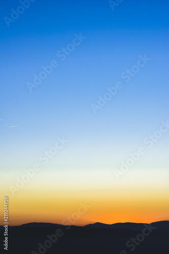 Sunset or sunrise background wallpaper photo of blue, orange and yellow sky over a horizont.