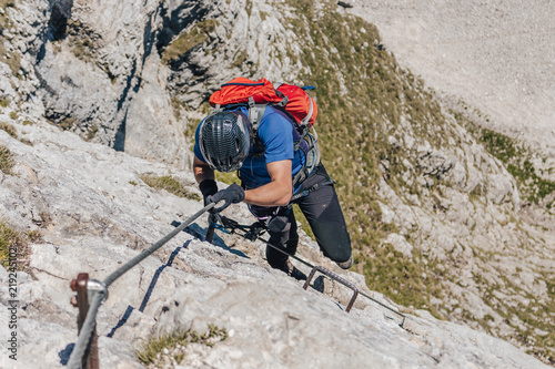 A climber climbing via ferrata. Adventure extreme ascent of an alpine rock wall. Summer mountain sport adventure. Man climbing ferrata.