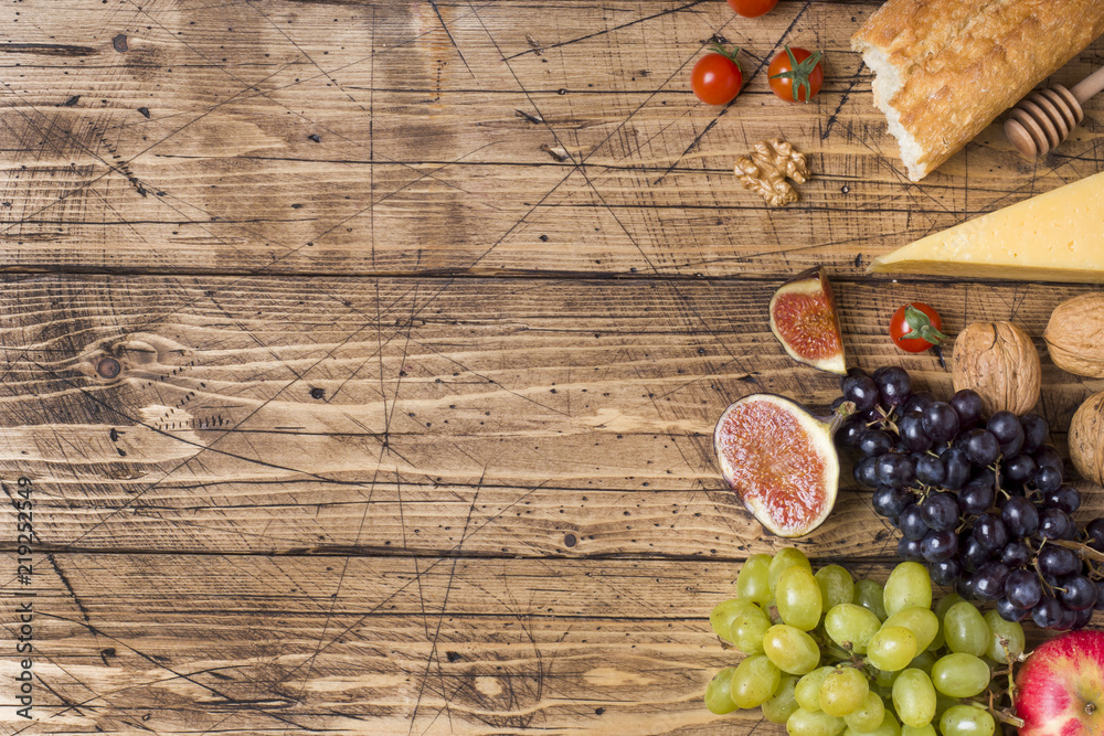 Cheese, wine, baguette grapes figs honey and snacks on the rustic wooden table top with copy space. Cheese, wine, baguette grapes figs honey and snacks on the rustic wooden table top with copy space.