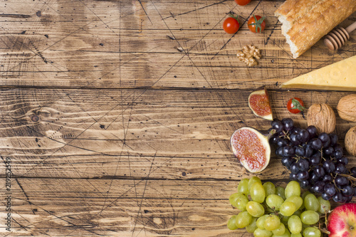 Cheese, wine, baguette grapes figs honey and snacks on the rustic wooden table top with copy space.