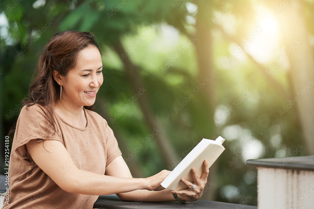 Mature Asian woman enjoying reading a book outdoors Mature Asian woman enjoying reading a book outdoors