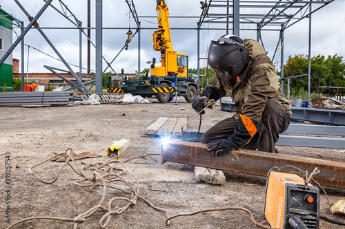 Canvas Print A strong man is a welder in brown uniform, welding mask and welders leathers, a