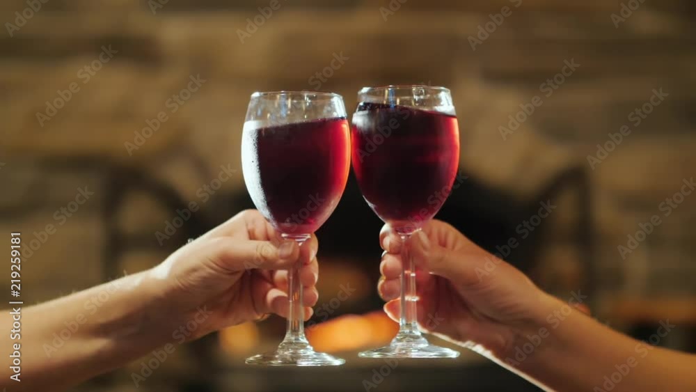 Two hands with glasses of red wine. Clinking against the background of a burning fireplace, celebrating in a cozy house the concept Two hands with glasses of red wine. Clinking against the background of a burning fireplace, celebrating in a cozy house the concept