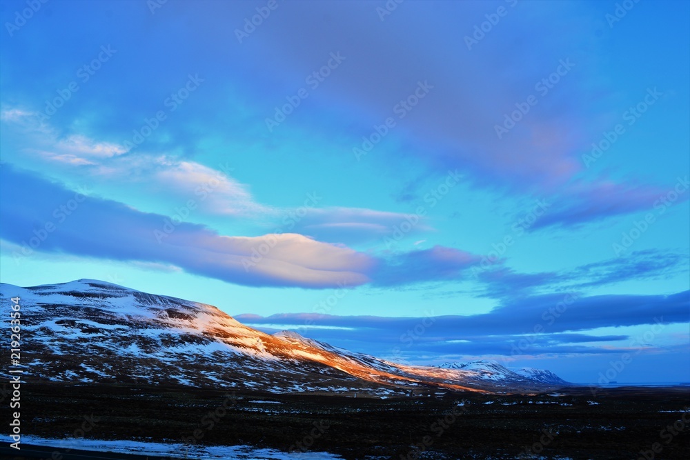 A beautiful sky in Iceland with orange sunlight shining onto a mountain