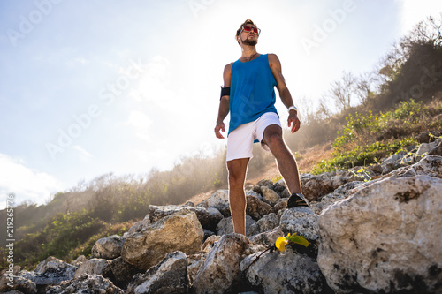 bottom view of athletic man standing on rocks with sunlight