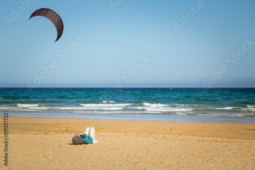 Woman lying down on sandy beach with calm water in Fuerteventura.