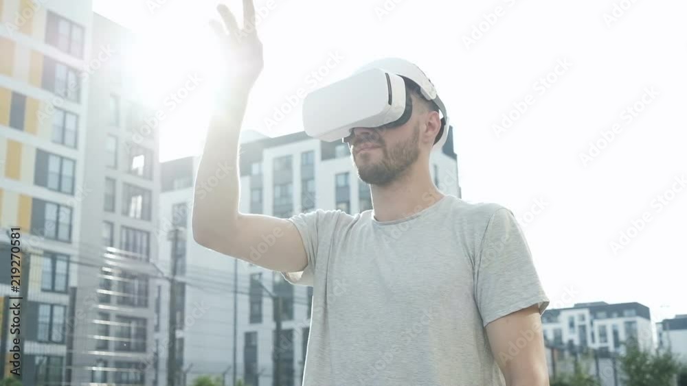 Man puts on vr glasses. Man using virtual reality headset outdoors. Future is now. Handsome man playing game in modern virtual reality glasses. Man puts on vr glasses. Man using virtual reality headset outdoors. Future is now. Handsome man playing game in modern virtual reality glasses.