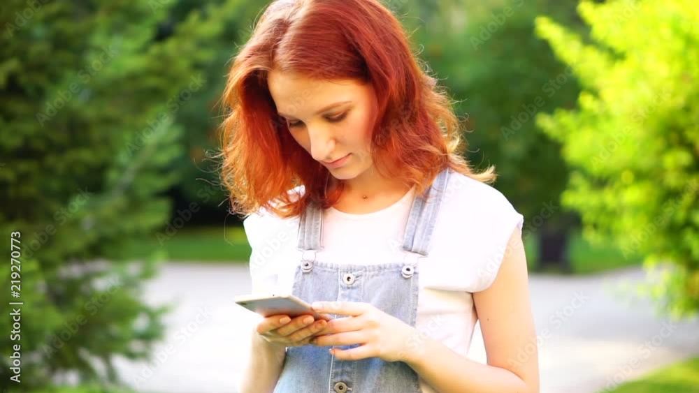 red-haired girl is writing a message in the phone red-haired girl is writing a message in the phone