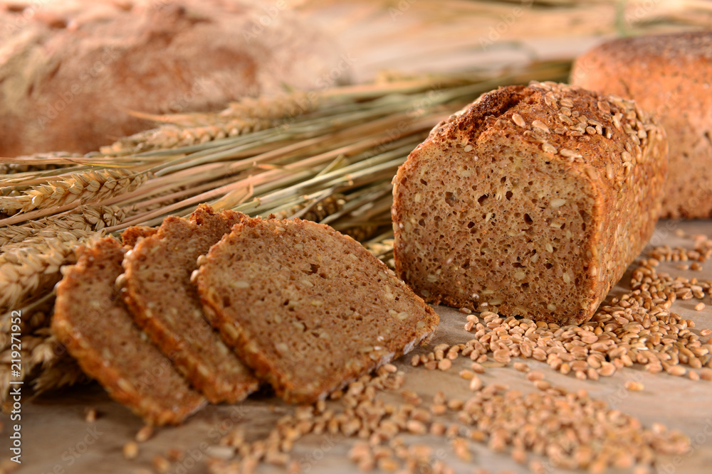Vollkornbrot mit Getreide, angeschnitten, Brotscheiben, mit Brotlaib im Hintergrund, auf Holzuntergrund