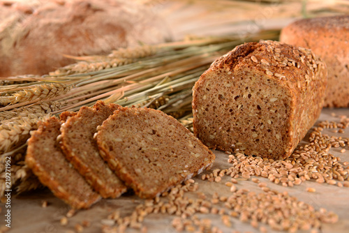 Vollkornbrot mit Getreide, angeschnitten, Brotscheiben, mit Brotlaib im Hintergrund, auf Holzuntergrund