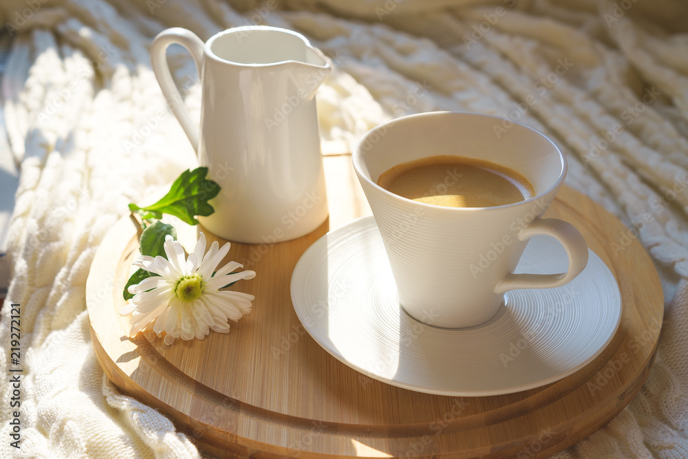 Top view on white cup of coffee with cozy knitted plaid on a round wooden desk and with white flower Top view on white cup of coffee with cozy knitted plaid on a round wooden desk and with white flower