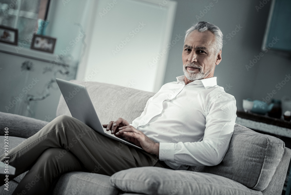 Freelance worker. Busy bearded man working with computer and sitting on sofa Freelance worker. Busy bearded man working with computer and sitting on sofa