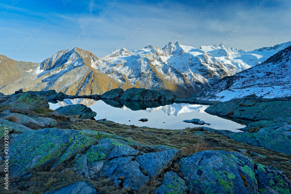Fototapeta premium Morning in Italian Alps, mountains with smaůe lake in the rock, hills in the clouds, Alp, Gran Paradiso, Italy. Mountain landscpe with blue sky with white clouds.