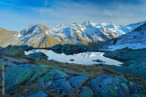 Morning in Italian Alps, mountains with smaůe lake in the rock, hills in the clouds, Alp, Gran Paradiso, Italy. Mountain landscpe with blue sky with white clouds.