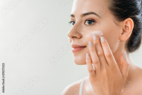 Fotografia beautiful smiling young woman applying face cream and looking away
