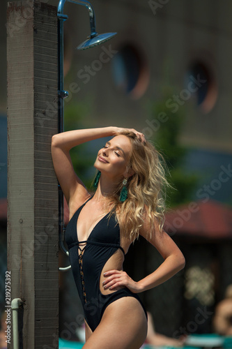 beautiful young girl in a black bathing suit sunbathing by the pool in summer