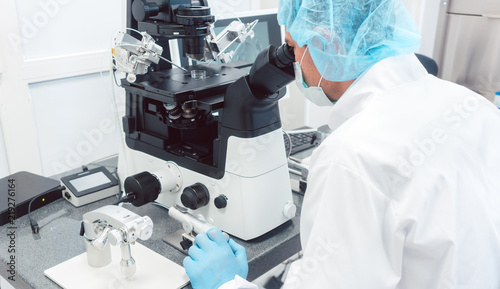 Quadro su tela Doctor or scientist looking thru microscope in biotech lab