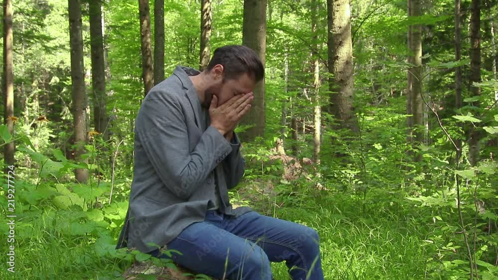 Sad desperate man praying in nature. Sitting on a tree in the forest. Christian religion Sad desperate man praying in nature. Sitting on a tree in the forest. Christian religion