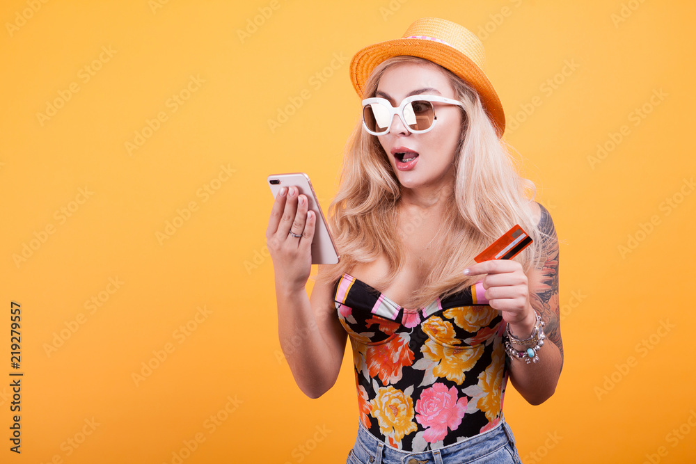 Happy attractive young woman holding and showing credit card in studio over yellow background Happy attractive young woman holding and showing credit card in studio over yellow background