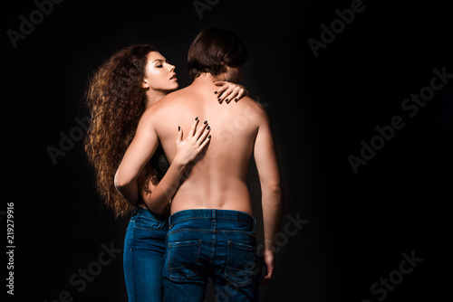back view of girlfriend hugging shirtless man isolated on black