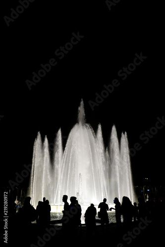Black and white photography. Silhouettes of people against the background of a fountain at night in the city
