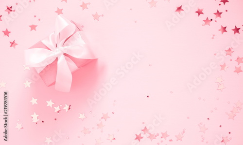 Festive pink background. Gift with satin bow and shining stars on light pink pastel background. Christmas. Wedding. Birthday. Happy woman's day. Mothers Day. Valentine's Day. Flat lay, top view 