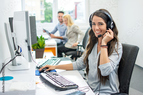 Smiling friendly female call-center agent with headset working on support hotline in the office photo