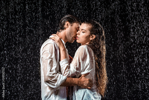 side view of couple kissing under rain isolated on black