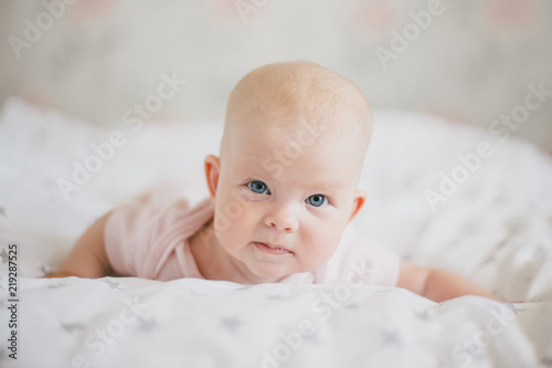 Little cute baby girl wearing pink suit smiling on a bed 