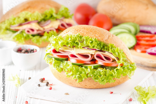 Closed sandwich in bun with ham, cheese, lettuce, tomato, cucumber, red onion. Delicious breakfast, classic lunch