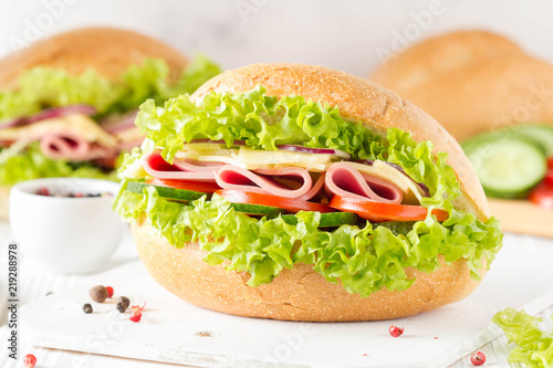 Closed sandwich in bun with ham, cheese, lettuce, tomato, cucumber, red onion. Delicious breakfast, classic lunch