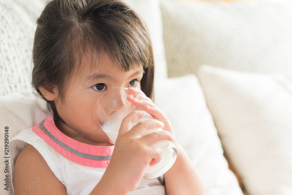 Happy little asian girl hand holding drinking milk glass, sitting on sofa at home. Medicine and health care concept. Happy little asian girl hand holding drinking milk glass, sitting on sofa at home. Medicine and health care concept.