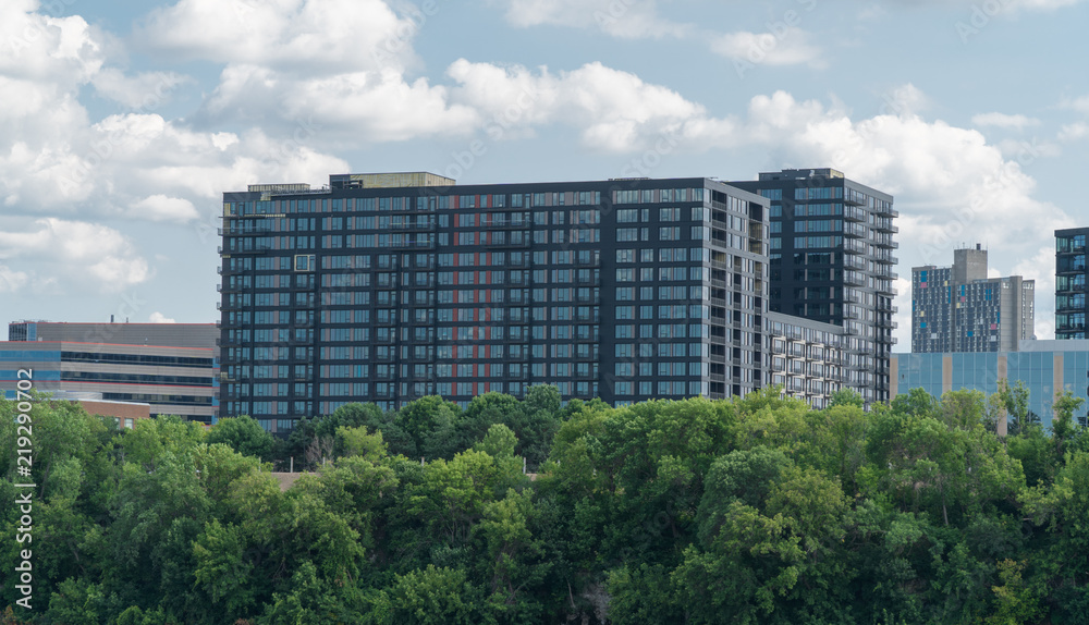 Wide view of luxury apartment building in big urban city. Exterior establishing shot during day time. Loft windows line the facade in modern cityscape view behind tree line park area