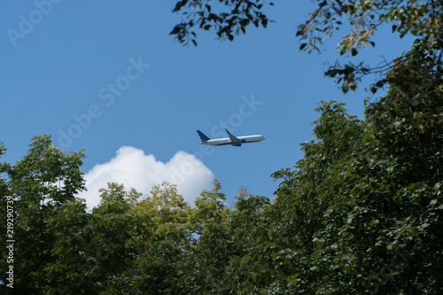 Commercial airline passenger jet flying high through the sky over park treeline just after takeoff from airport. Clear weather and blue skies make for reliable air traffic and transportation