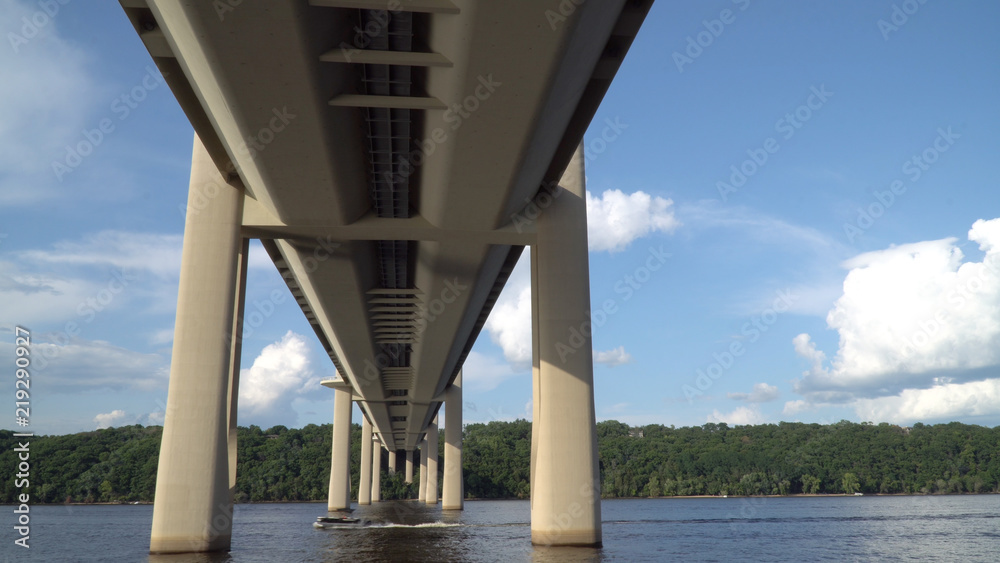 View from boat passing underneath bridge spanning over a river on a clear summer day. Modern construction engineering for road motorway to cross natural borders