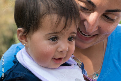 Bilde på lerret Beautiful young infant baby girl and mommy sit outside in a park smiling having lots of fun in the summer weather together