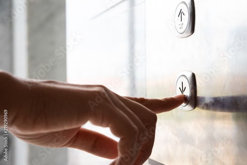 Close up waman hand press a down button of elevator inside the building for upper high level floor. photo