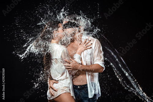 portrait of man with black ribbon on eyes hugging sexy girlfriend near by while swilled with water isolated on black