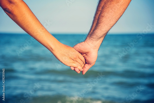 A man holds a woman by the hand on the beach by the sea, the concept of family, love and peaceful life.