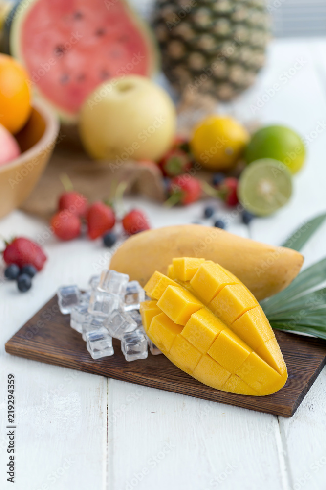 Ripe Mango on a wooden plate with ice cubes and fruit as background