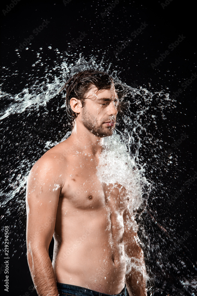 Fototapeta premium side view of young man with water splash isolated on black