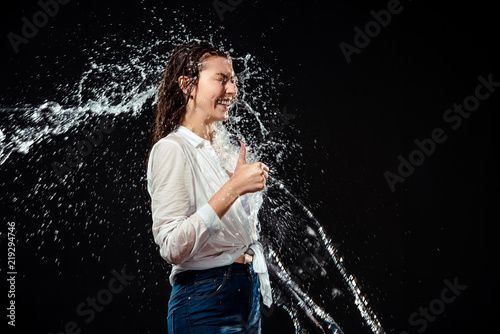 side view of smiling woman in white shirt showing thumb up while swilled with water isolated on black